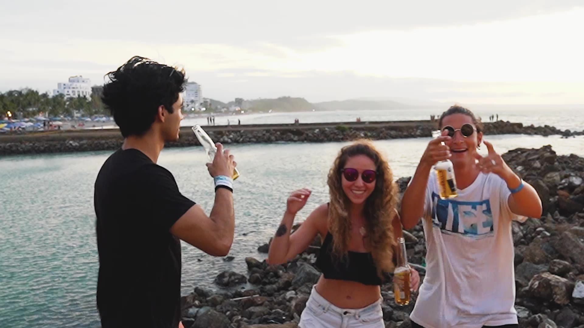 Amigos con cervezas bailando sobre las rocas frente al mar