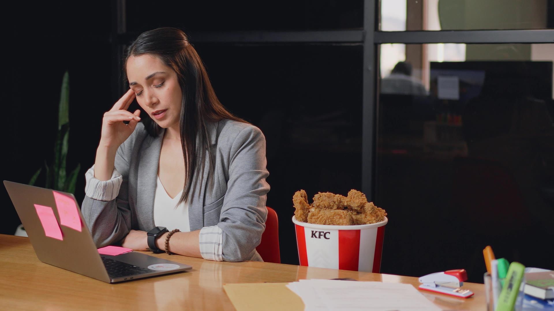 Mujer agotada en la oficina con un bucket de KFC en el escritorio