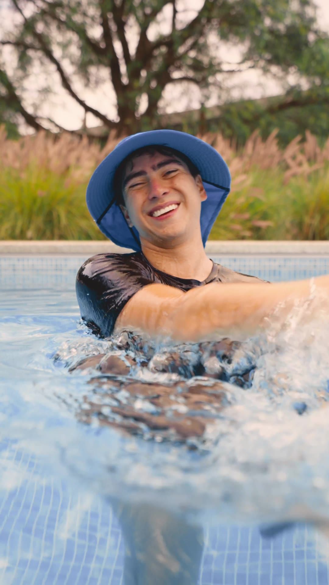 Joven con sombrero de pescador riendo dentro de la piscina
